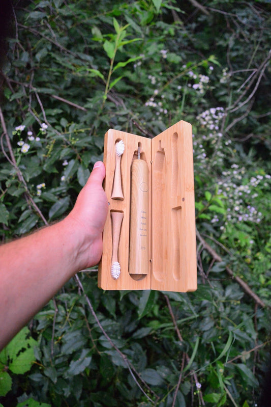Open bamboo electric toothbrush travel case held in hand, holding the sonic handle and two plant-based brush heads