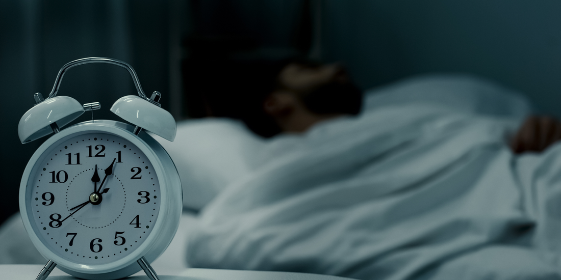 A man sleeps in the background as an alarm clock reads just after midnight