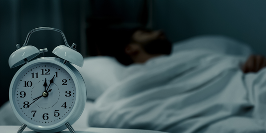 A man sleeps in the background as an alarm clock reads just after midnight