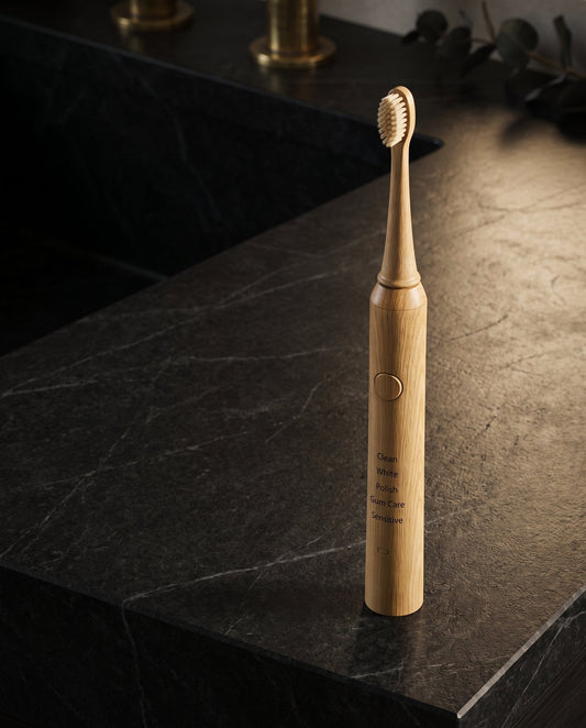 A bamboo sonic electric toothbrush sits on a dark stone counter Vearthy.com