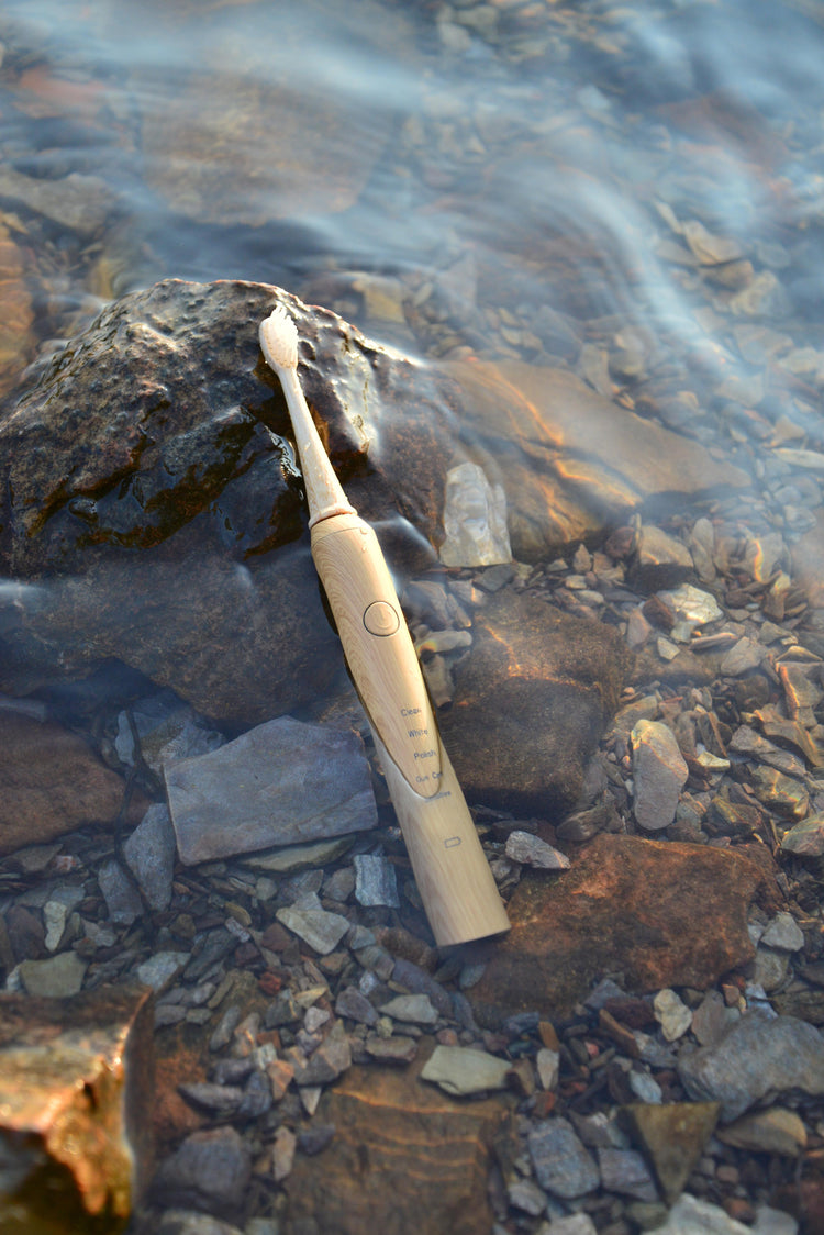 A waterproof bamboo sonic electric toothbrush from Vearthy, sits half submerged in the shallows of a clear lake