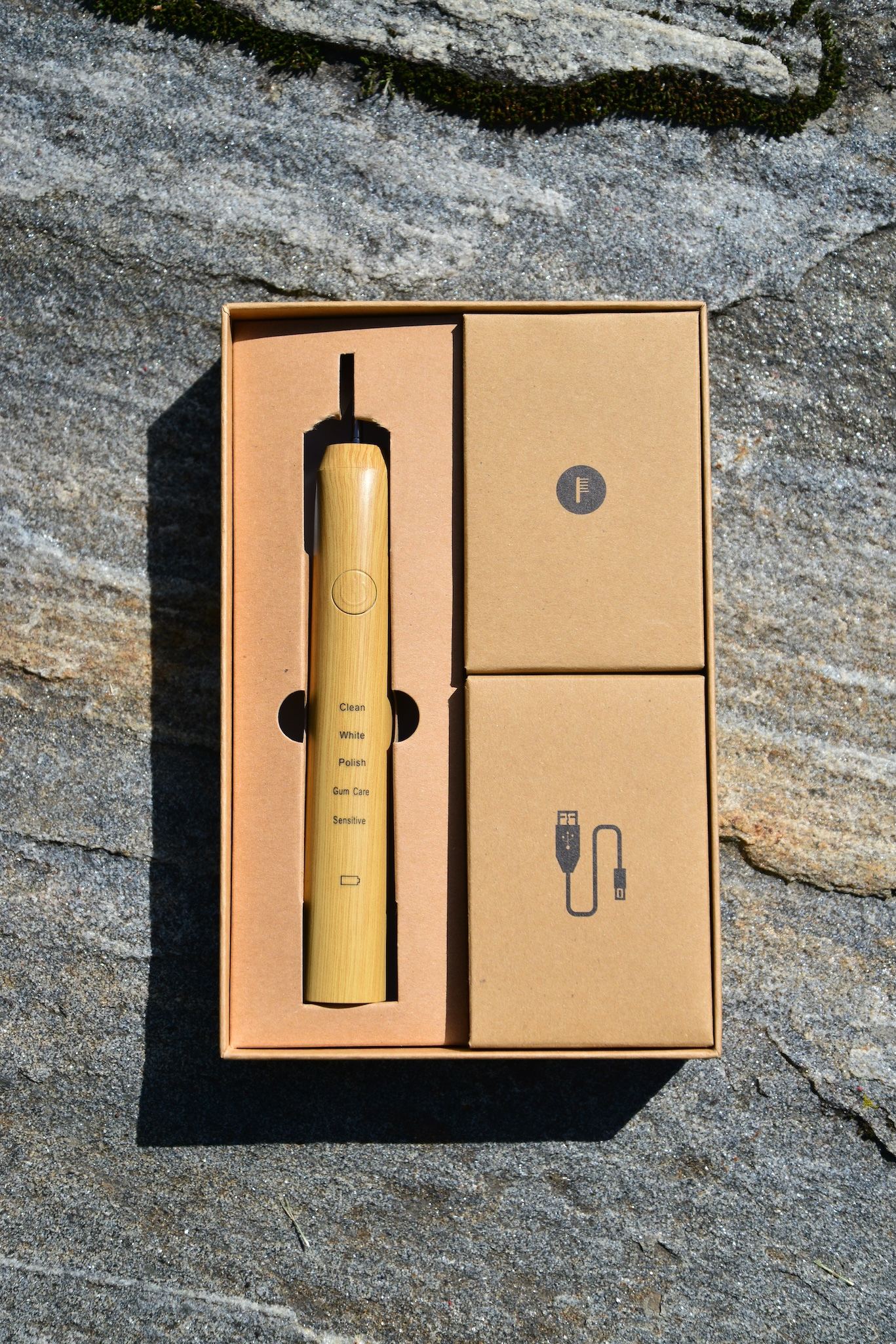 Vearthy electric toothbrush retail box open on stone, showing the bamboo-look sonic handle, brush head and USB charging cable