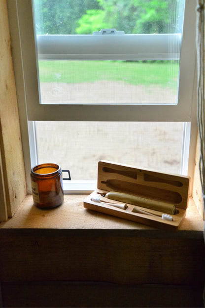 Bamboo electric toothbrush travel case open on a sunlit windowsill beside an amber glass candle