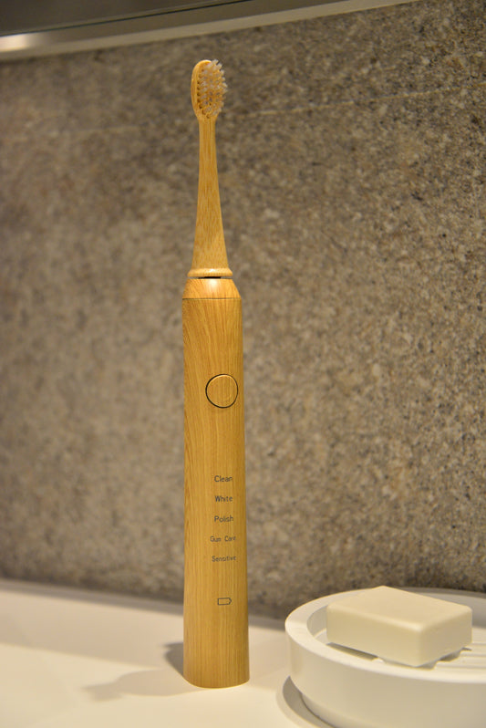 Bamboo electric toothbrush on a bathroom counter with soap in the background