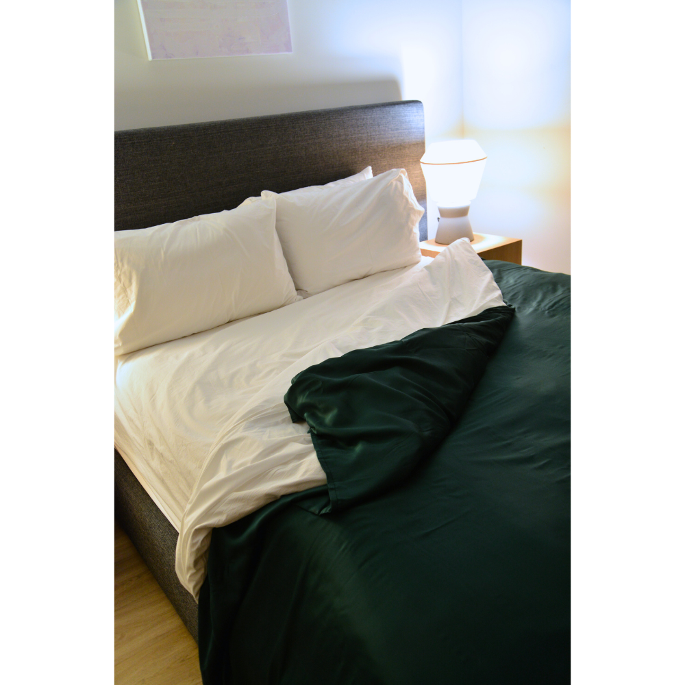 Bed with white bedding and a forest green duvet cover in a bedroom setting.