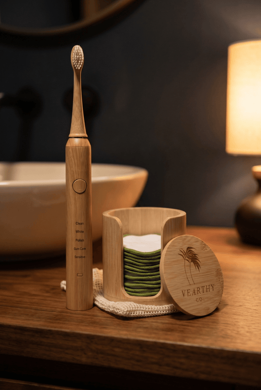 A bamboo electric toothbrush stands on a wooden bathroom counter beside a matching bamboo tooth holder with green-and-white reusable pads and a round lid engraved with the brand name Vearthy