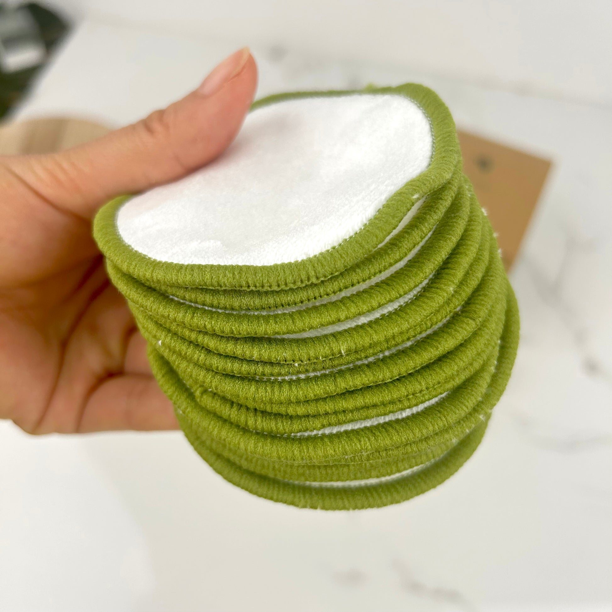 Close up of a stack of green soft reusable bamboo face pads held by a hand with a white background