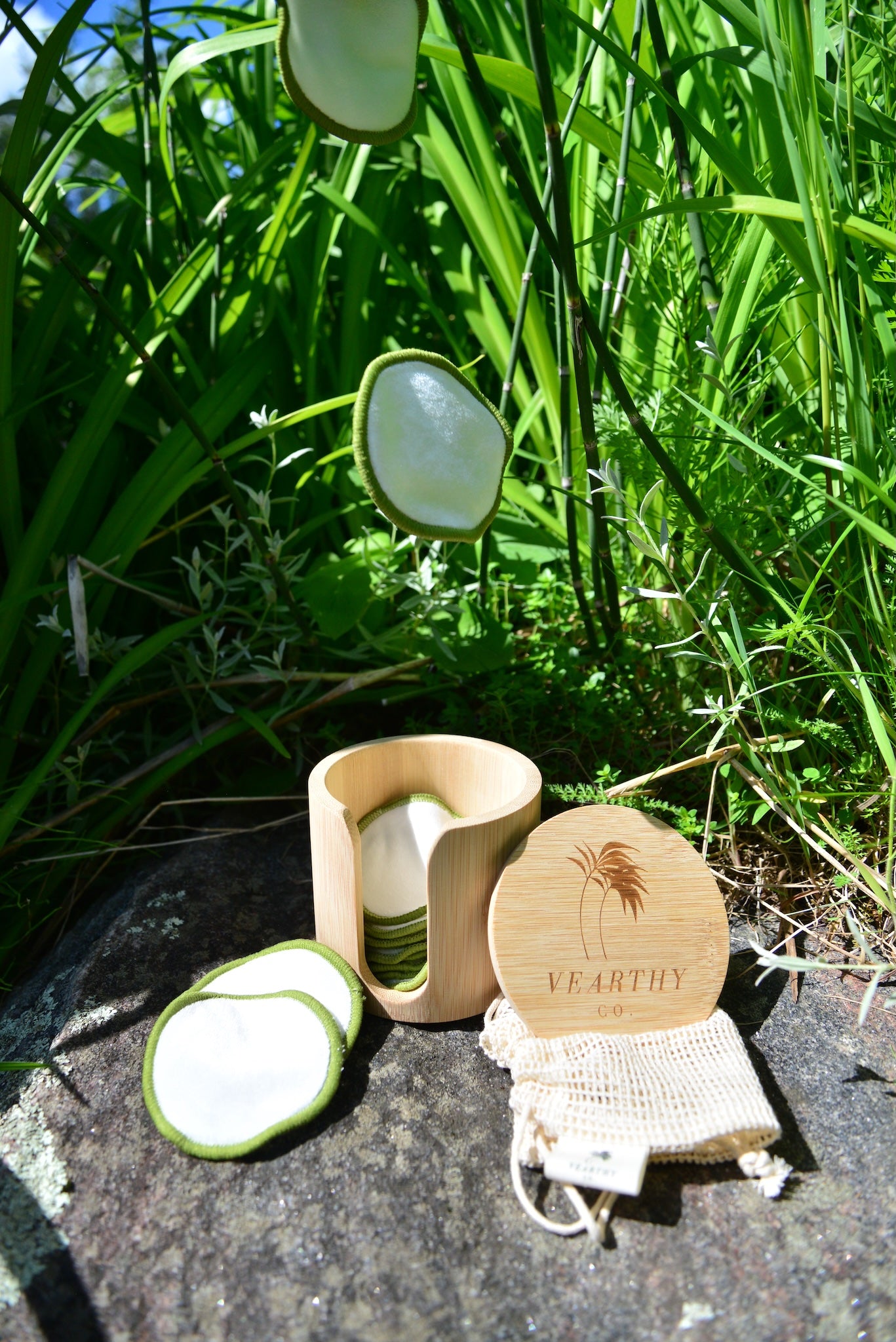 Two Vearthy bamboo cotton face pads falling into the bamboo holding case on a rock.