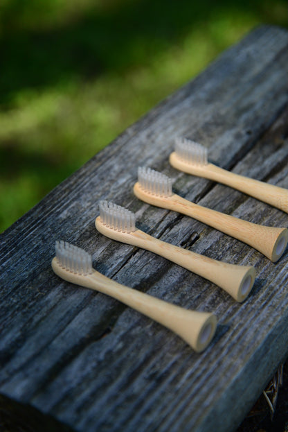Four bamboo electric toothbrush heads lined up diagonally on a dark, weathered wooden surface