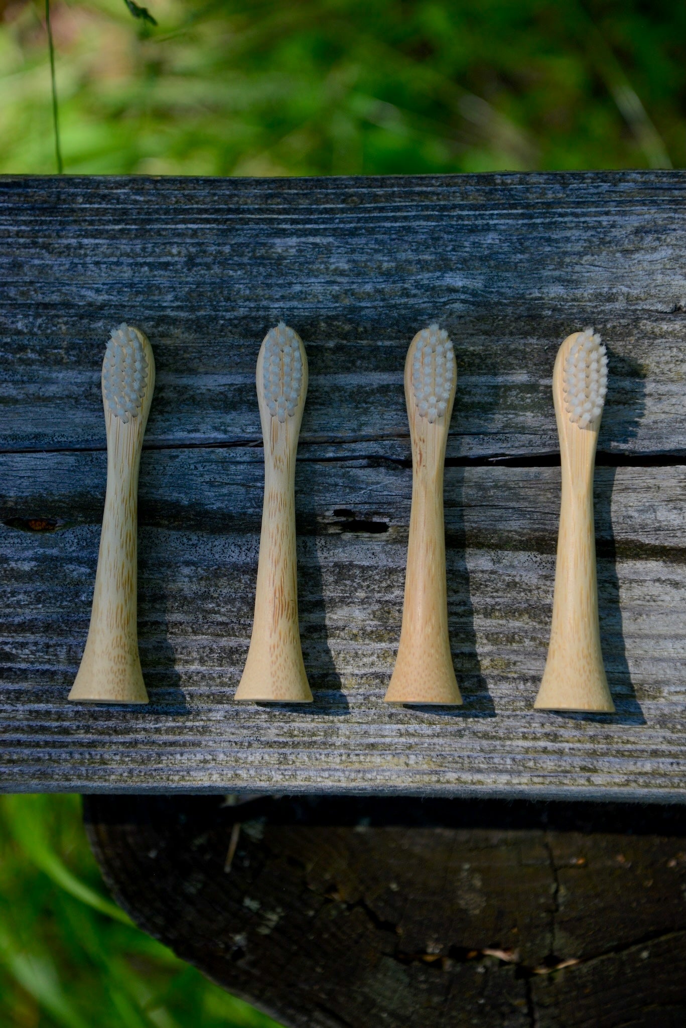 Four bamboo electric toothbrush heads lined up horizontally on a dark, weathered wooden surface