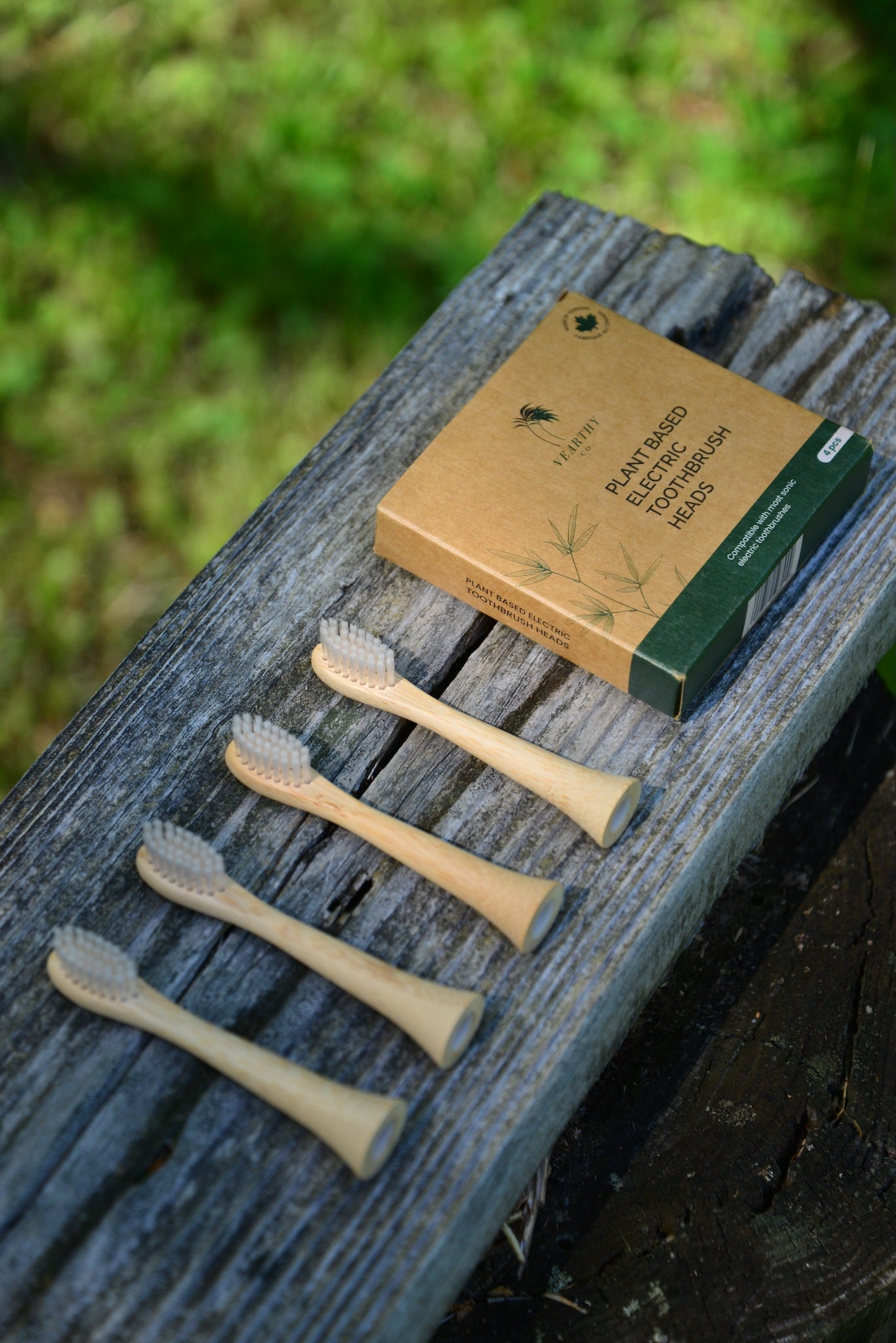 Vearthy plant based toothbrush retail box next to four bamboo replacement heads with castor seed oil bristles on a weathered log